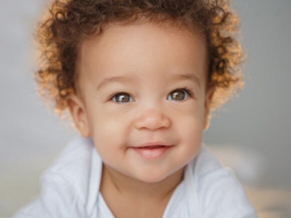 Bebé con cabello rizado sonriente mirando la cámara