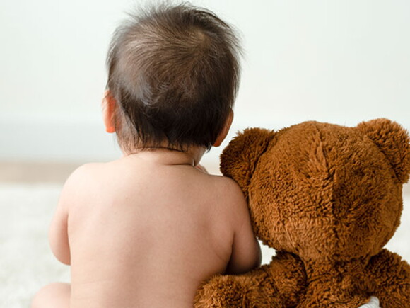 Bebé con pañal de espalda junto a un oso de peluche