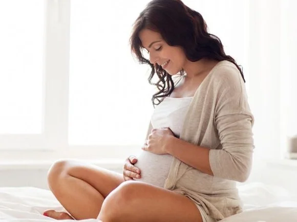 Mujer embarazada con top blanco y cárdigan sujetando su barriga de embarazada