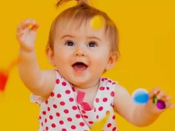 Bebé agarrando confeti delante de un fondo amarillo