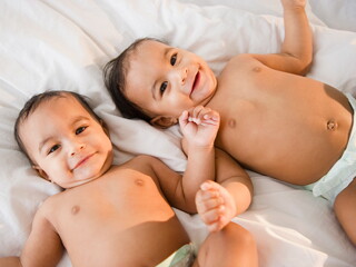 Bebés gemelos sonriendo acostados en la cama. 