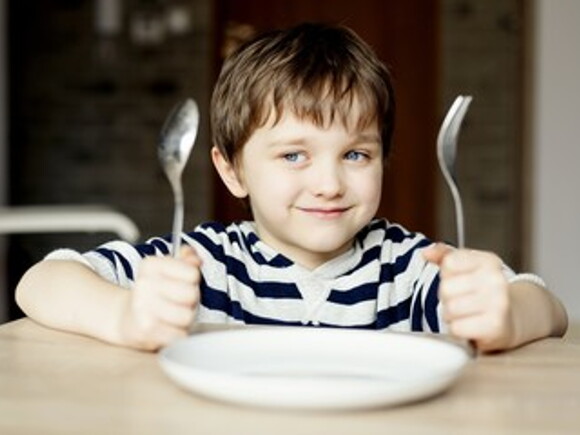 Niño alegre con cuchillo y tenedor esperando la comida
