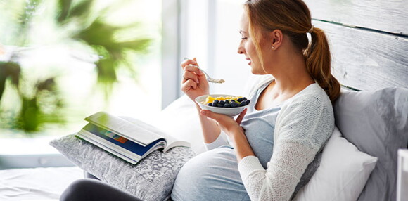 Mujer embarazada sentada comiendo frutas.