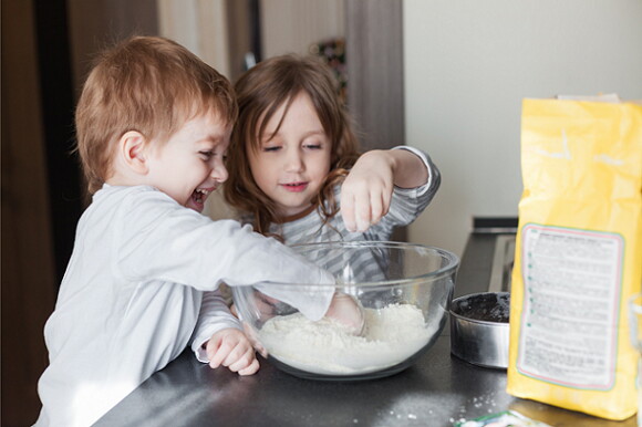 niño y niña cocinando juntos en un bol lleno de harina