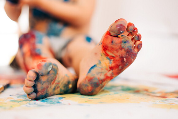 niño con los pies pintados realizando dibujos sobre papel en el suelo